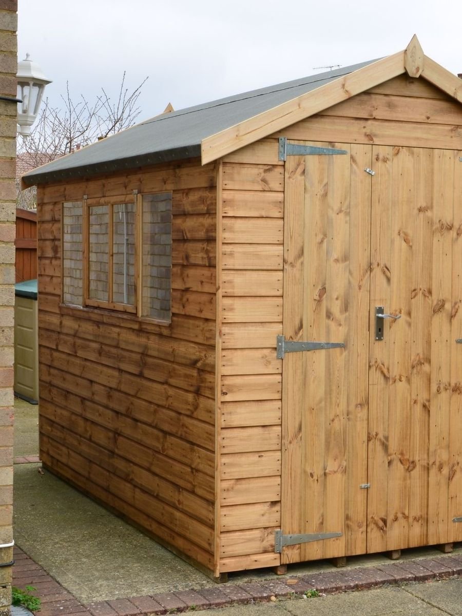 Abri de jardin en bois avec double porte et fenêtre, posé le long d'une maison