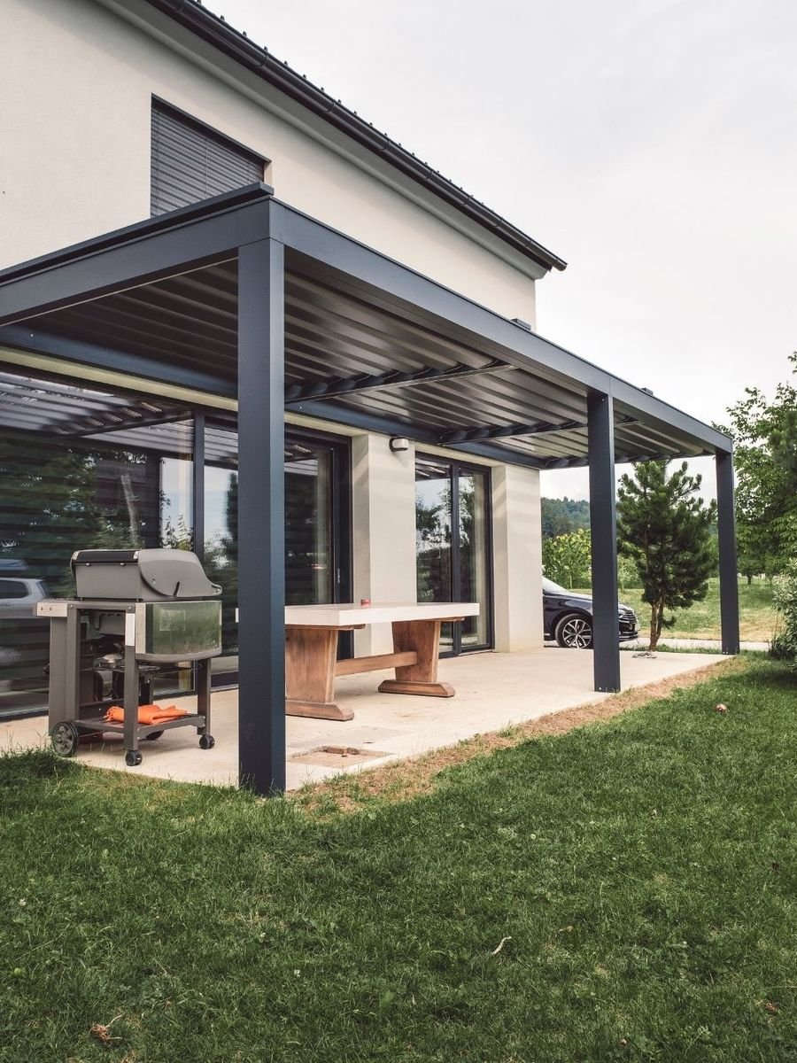Pergola bioclimatique en aluminium adossée à une maison, au-dessus d'une terrasse